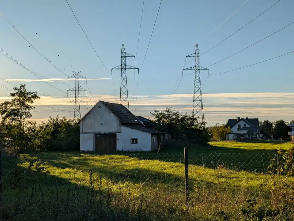 Linie wysokiego napięcia nad domem i łąką na wsi